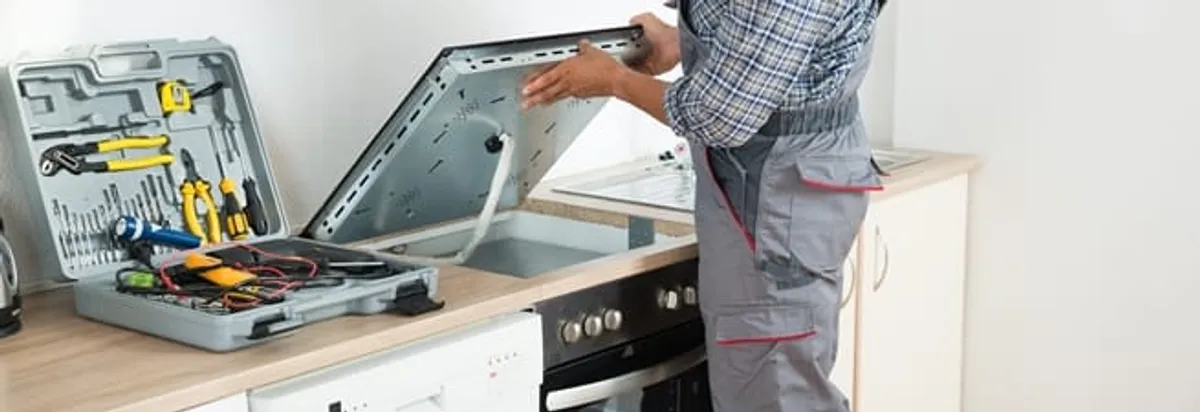 Cooktop repair technician lifting a built-in stovetop for service in Marietta, GA