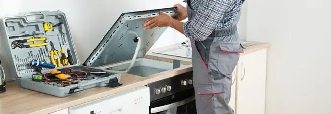 Cooktop repair technician lifting a built-in stovetop for service in Marietta, GA