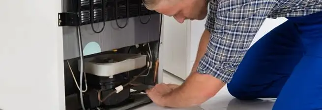 Refrigerator repair technician servicing the compressor and condenser area in Marietta, GA