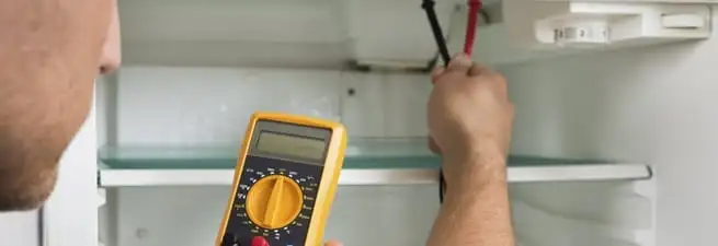 Refrigerator repair technician testing electrical components with a multimeter in Marietta, GA