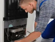 Refrigerator repair technician servicing the compressor and condenser area in Marietta, GA